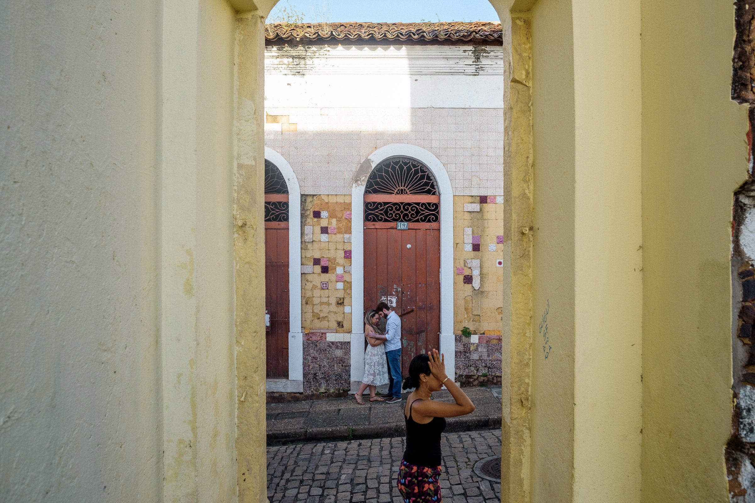 Casal se abraçando na frente de um casarão colonial com azulejos coloridos.